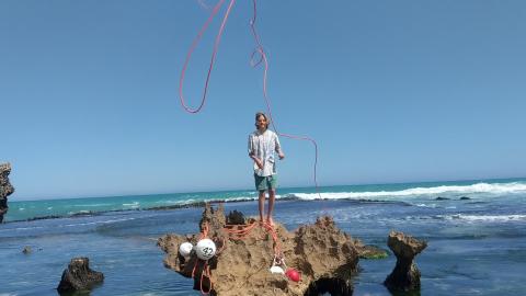 teen tossing rope to beach from rocks