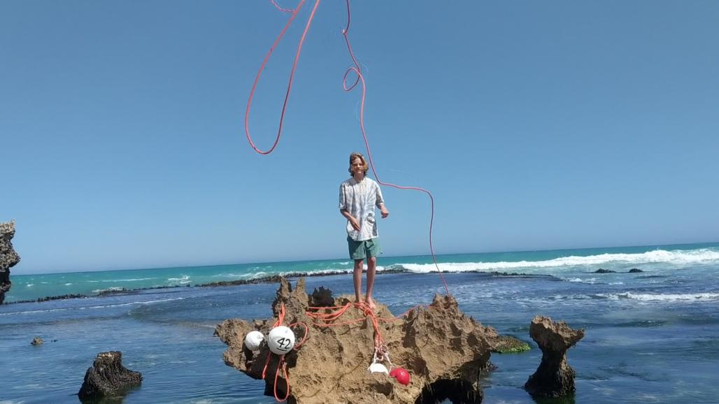 teen tossing rope to beach from rocks